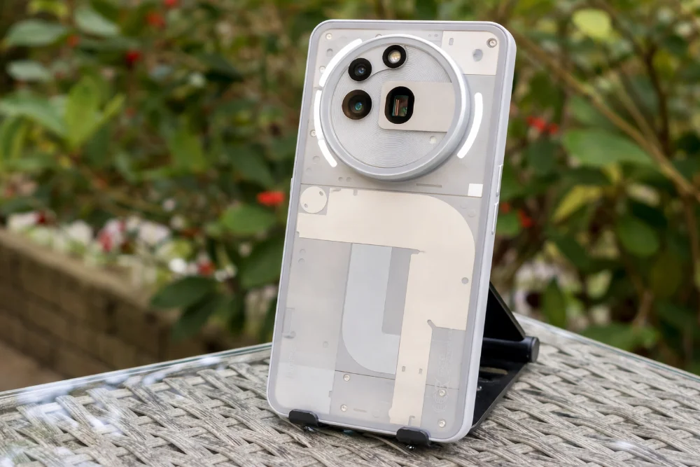 Nothing Phone (4a) — дизайн задней панели и камера смартфона вблизи Смартфон Nothing Phone (4a) с прозрачной задней панелью и круглым блоком камер на столе на улице, фирменный дизайн Nothing, четкое освещение, детальный вид корпуса