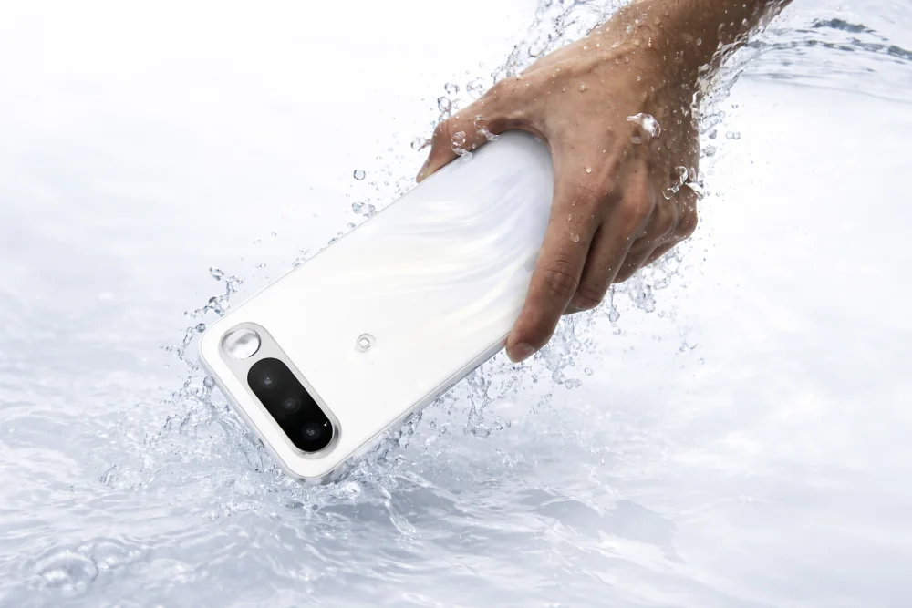 Realme 16 5G с батареей 7000 мА·ч — защита от воды и прочный корпус Смартфон Realme 16 5G белого цвета в руке под водой, крупный план корпуса с двойной камерой, брызги воды и яркое освещение, демонстрация влагозащиты и прочности устройства